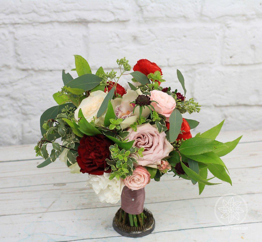 Bridesmaid's bouquet in a garden style of red roses and ranunculus, mauve roses, pink spray roses, orchids, and scabiosa, complimented by lush greens. large , lush, loose , romantic , garden style , fragment, blush roses, burgundy dahlias, white roses, astilbe, white orchids, berries and euc.